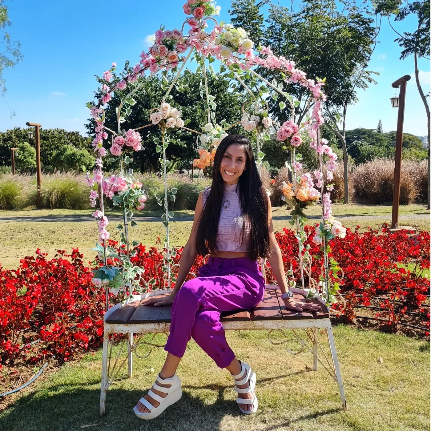 Carol sentada num banco de jardim cercado de flores