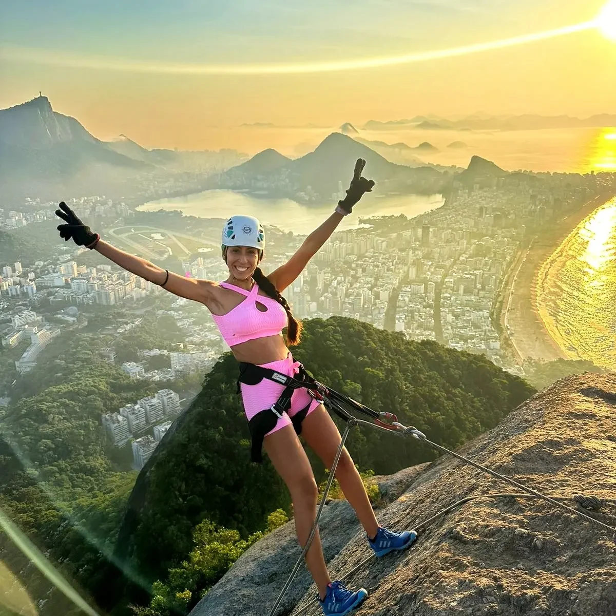 Carol descendo de rapel por uma formação rochosa com vista para a costa