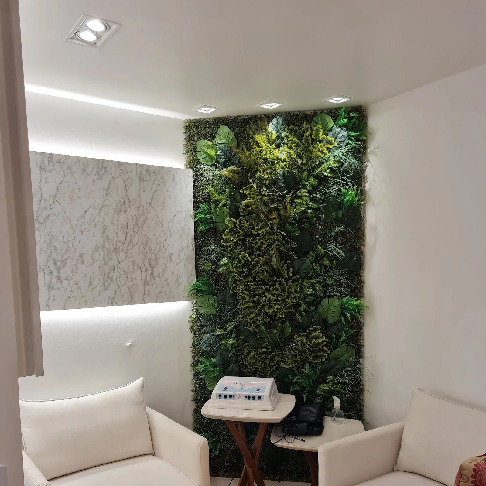 Recepção da clínica com poltronas claras e parede verde de plantas