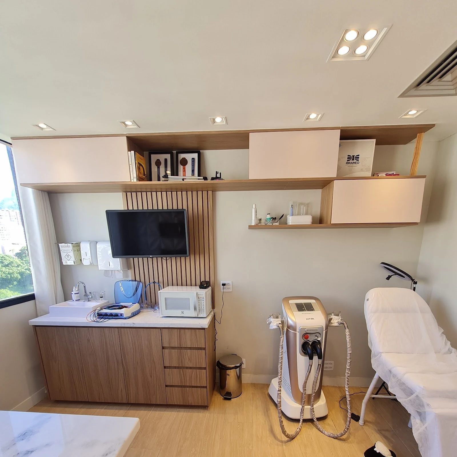 Sala de atendimento com maca branca, bancada de mármore e aparelhos de estética